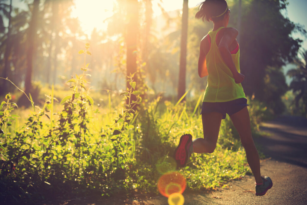 Junge Läuferin im Wald mit Sonnenstrahlung